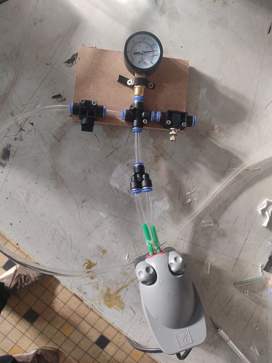 Montage complet : pompe NW33 reliée par un raccord 2 en 1 à un raccord 4 voies fixé sur une plaque de MDF, avec le vacuomètre, un robinet et la vis de fuite